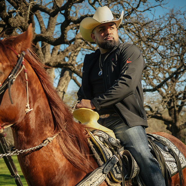 A man, Louie The Singer, dressed as a cowboy, riding a red horse.